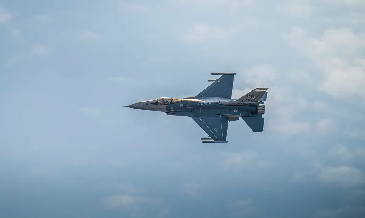 Military F-16 jet flying against a backdrop of clouds, showcasing aviation power.