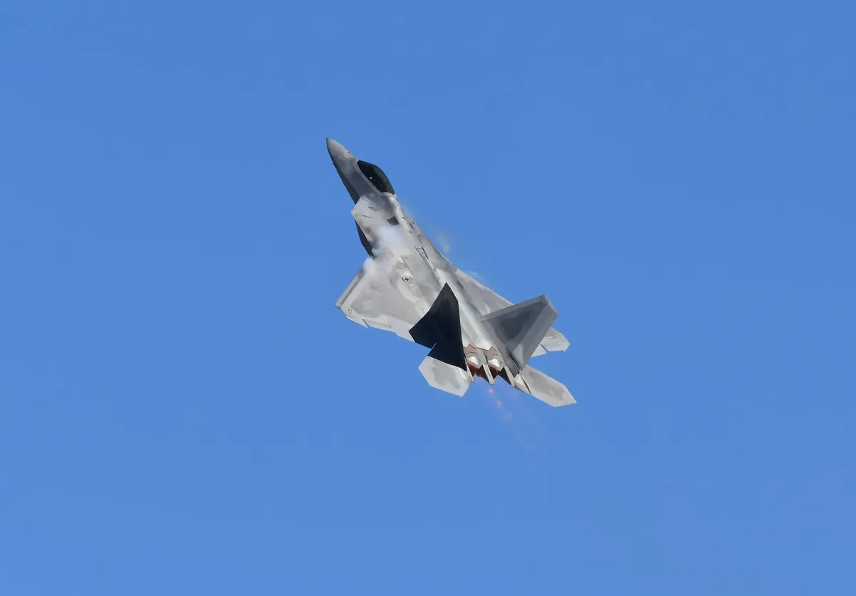 Military jet fighter captured during a dynamic aerial performance against a clear blue sky.