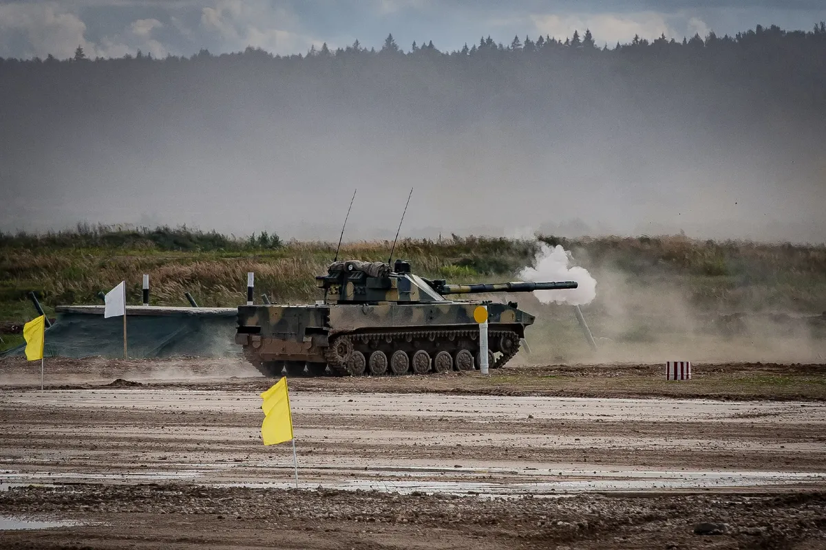 A military tank firing a shell during training in an open field.